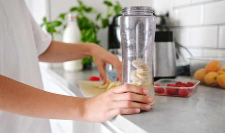 Little Girl Adding Bananas To A Milkshake In The Kitchenの写真素材