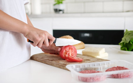 Little Girl Cutting A Tomato On The Board With A Knife In The Kitchenの写真素材