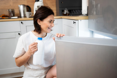Joyful Woman In The Kitchen Getting A Milk Bottle From The Fridgeの写真素材