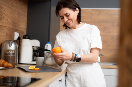 Happy Girl Cutting A Fresh Orange For Breakfast In The Kitchenの写真素材