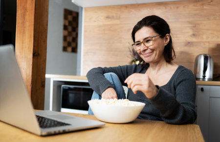 Girl Laughing Watching A Movie On Laptop And Eating Popcornの写真素材
