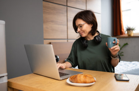 Freelance Girl Working At Home On A Computer While Having Breakfast In The Kitchenの写真素材