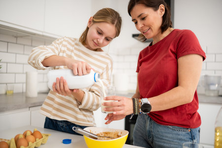 Happy Little Girl And Mother Baking In The Kitchen And Pouring Milkの写真素材
