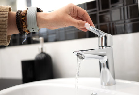 Girl Opens The Bathroom Sink Mixer Tap And Water Flows From The Faucetの写真素材