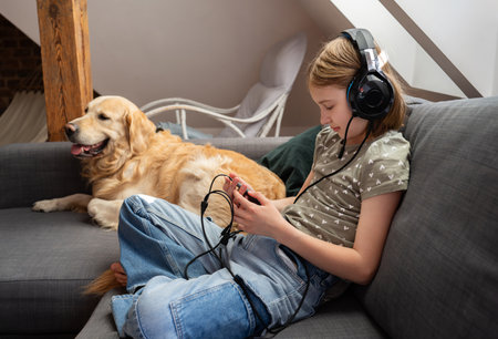 Cute Little Girl Using Smartphone, In Headphones With Dog At Homeの写真素材