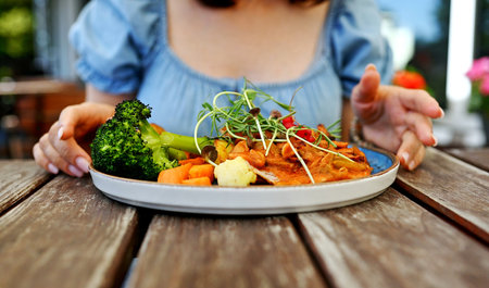 Girl Eating Vegetable Dish At Street Restaurant And Meat With Potatoes And Broccoliの写真素材