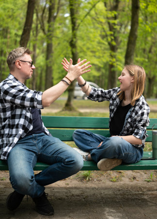 Happy Father And Little Daughter Sitting On A Bench Giving A High Five In Family Lookの写真素材