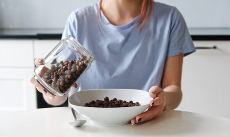 Girl Pouring Brown Cereal Balls Into A Plate For Breakfast