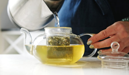 Girl In The Kitchen Filling A Teapot With Hot Water From A Kettle For Green Teaの写真素材