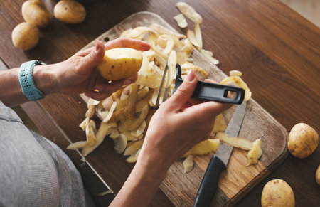 Top View Of A Woman Peeling Raw Potatoes With A Potato Peeler And Other Raw Vegetables