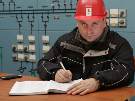 Engineer with red helmet writing data in the power plant control centerの写真素材