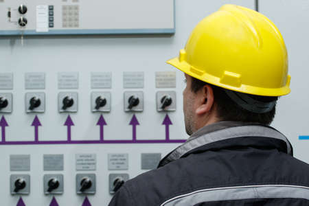 Engineer in yellow helmet reading instruments in power plant control center