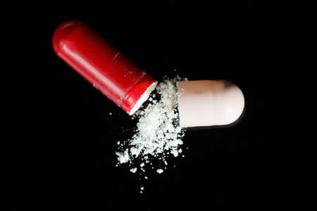 Broken red and pink antibiotic capsule on black top vuewの写真素材