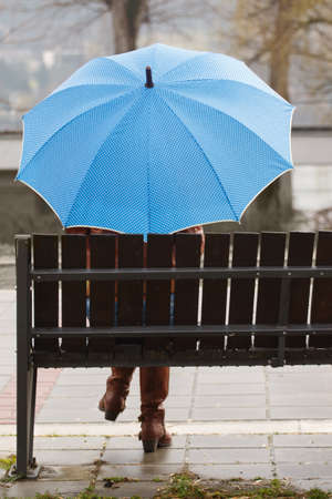 Rainy day  woman siting on bench and holding blue umbrellaの写真素材