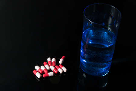 Red and pink antibiotic capsule and glass of water  on black