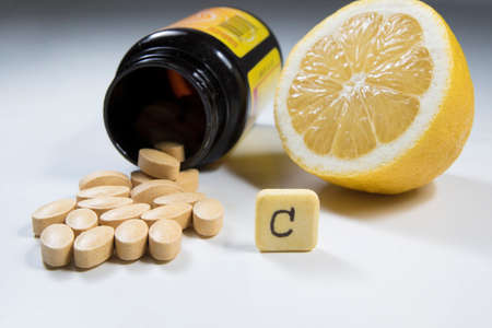 vitamin c pills in a plastic bottle and lemon on whiteの写真素材