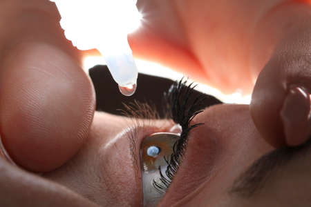 Closeup of young woman applying eye drops