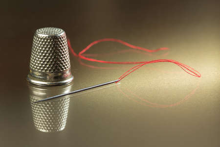 Needle, thread and red thimble on golden backgroundの写真素材