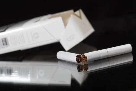 Broken cigar and empty box of cigarettes on the blackの写真素材