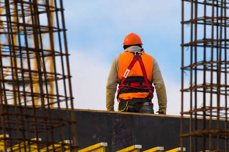 Climber dressed in orange with safety belt on construction site over blue skyの写真素材
