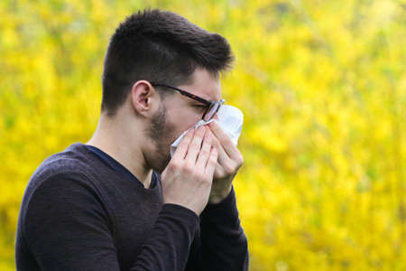 Boy with polen allergy over yellow flowers is sneezingの写真素材