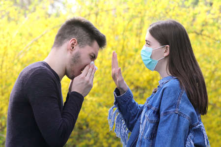 Stop the flu epidemy, Girl with protective mask and sneezing boy in the floral parkの写真素材