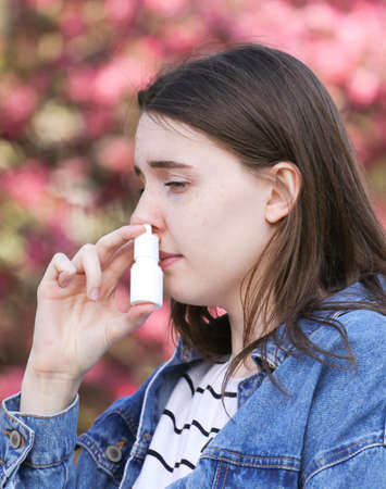 Teenager girl using nose inhaler in park over pink flowerの写真素材