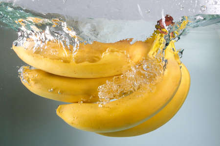 Bunch of yellow ripe bananas splashing in water on whiteの写真素材