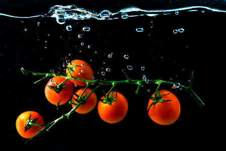 Red ripe cherry tomatoes under water with bubles on blackの写真素材