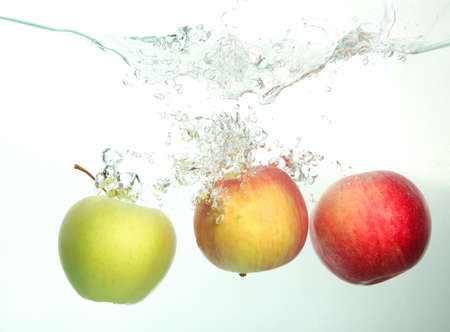 Three apples red, green, and yellow splash in water on whiteの写真素材