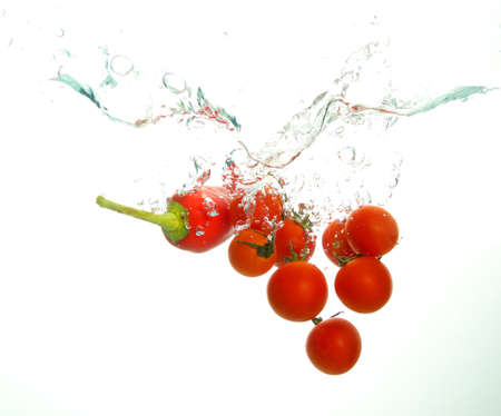 Red ripe cherry tomatoes and paprika under water with bubles on whiteの写真素材