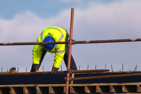 Worker with blue helmet knitting metal rods bars into framework reinforcementの写真素材