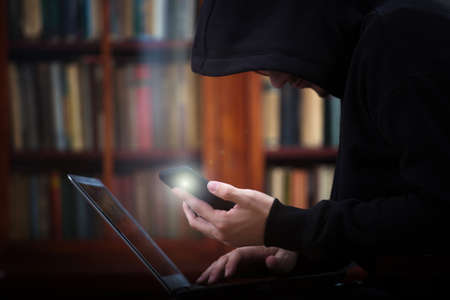 Hacker stealing password and identity with cell phone and laptopの写真素材
