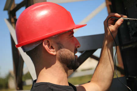 Engineer in red helmet with multimeter on the electric poleの写真素材