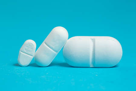 Three white  tablets of different sizes on blue, dosage