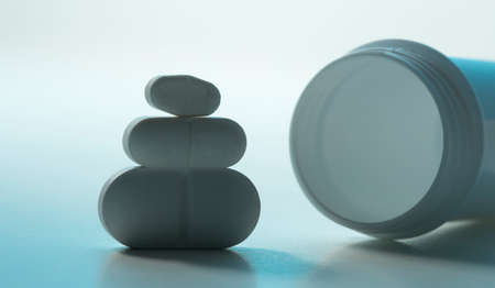 Three white aspirin pills of different sizes and plastic bottleの写真素材