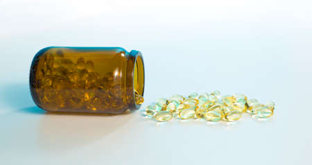 Shiny yellow Vitamin D fish oil capsule and  brown  glass bottle on white