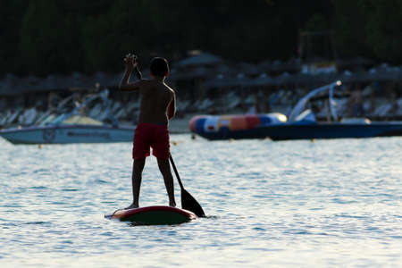 Boy addleboarding on the sunset in the beachの写真素材