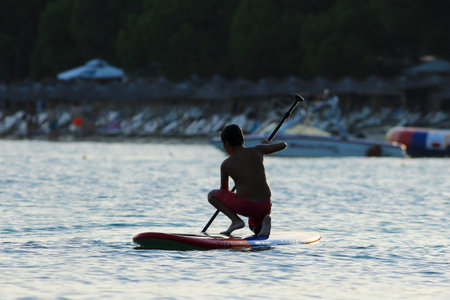 Boy paddleboarding on the sunset in the Kokonaries beach in Greece