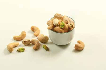 Group of hulled salty roasted cashews and pistachio nut in a white cup on whiteの写真素材