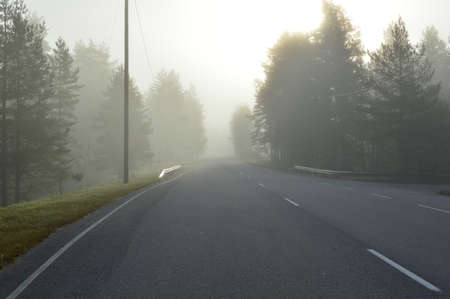 Foggy open road in Finland, the sun is shining from behind a veil of fog.の写真素材