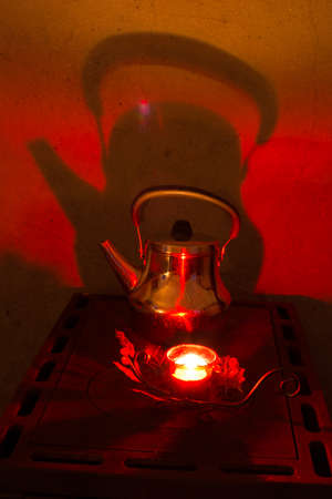 Coffee pot and  candle light on the top of the wood burning stove. candle and kettle makes shadows to stove flue.の写真素材