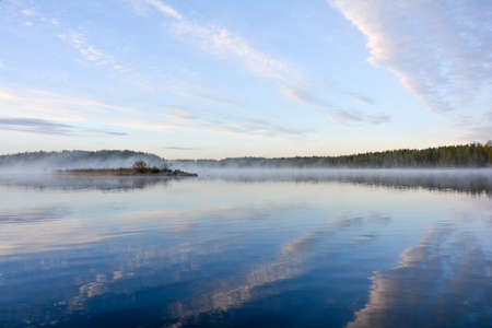 Early morning fishing trip to lake. Calm lake and clouds. Islet with few bushes.の写真素材