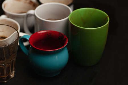 Dirty multi-colored cups, mugs, glasses after different types of coffee on a black wooden table left after morning coffee drinking , coffeeshop styleの写真素材