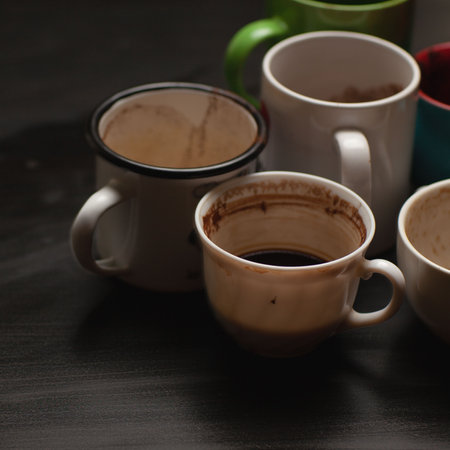 Dirty multi-colored cups, mugs, glasses after different types of coffee on a black wooden table left after morning coffee drinking , coffeeshop styleの写真素材