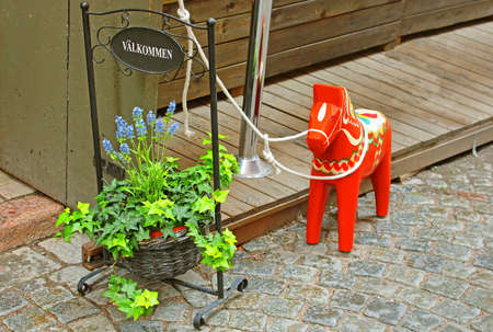 Inscription \"Welcome\", flowers and a hand-made traditional wooden Dalecarlian Horse (symbol of Swedish Dalarna and Sweden in general) at the entrance to the little shop in Gamla Stan, Stockholm, Swedenのeditorial素材