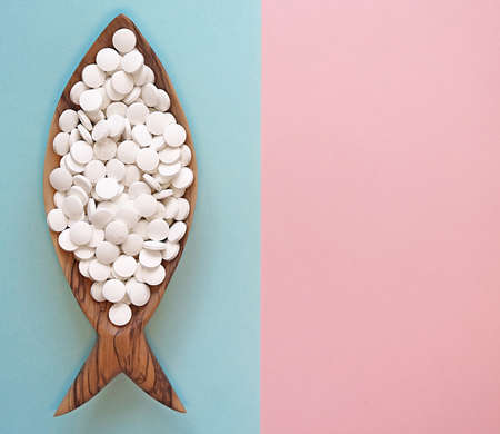 Calcium pills in a wooden dish in the form of a fish. Fish is rich in calcium. Color background....