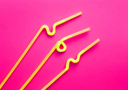 Yellow plastic cocktail tubes with a flexible part, due to which they can be twisted into a knot or in a zigzag, on a crimson background. Modern and trendy colors. Eco conceptの写真素材