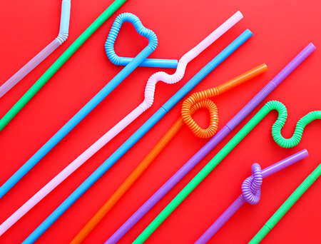 Colour plastic cocktail tubes with a flexible part, due to which they can be twisted into a knot or in a zigzag, or a heart shape, on a red background. Modern and trendy colors. Eco conceptの写真素材