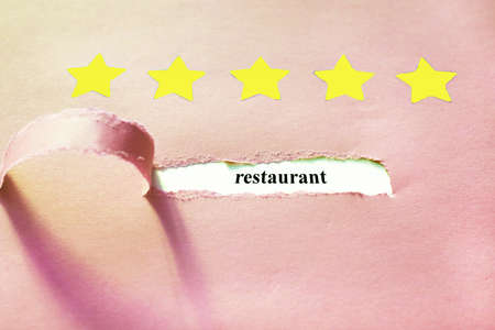 Oblong torn hole from right to left in pink sheet of paper with shadow and paper curl. White resulting background with word RESTAURANT. Yellow stars. Review concept. Copy spaceの写真素材